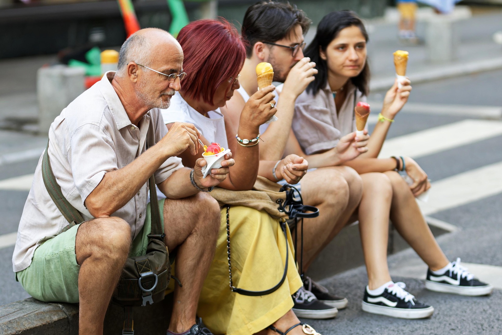 Vier Personen einer Reisegruppe sitzen entspannt am Straßenrand und genießen Eis, mit fröhlicher, sommerlicher Stimmung in urbaner Umgebung.